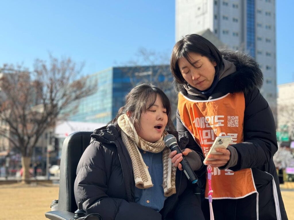 24년 12월 23일 강동구청 규탄 기자회견에서 진성선 활동가가 발언을 하고 있다. 김보연 활동가가 마이크 들길 조력하고 있다.