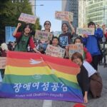 [사진 1] 2026년 10월 17일 불평등한 세계에 맞서, 1017 빈곤철폐 퍼레이드에 참석한 장애여성공감 활동가들의 단체사진. 장애여성공감의 무지개 깃발을 펼치고, ‘가난하고 돌봄받는 장애여성의 힘으로! 빈곤 철폐! 평등 쟁취!’ 구호가 적힌 피켓을 들고 있다. 한국어, 일어, 영어, 중어로 적었다.